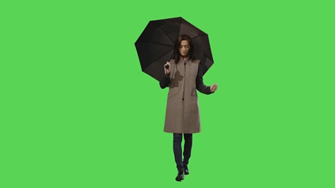 休闲的黑发女性在走路时注意到雨，并在背景的模拟绿色屏幕上打开雨伞。