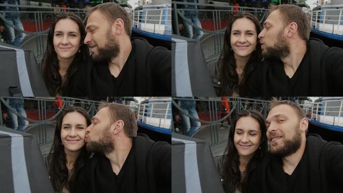 幸福的情侣自拍，视点拍摄。恋爱中的男人和女人在镜头前微笑，亲吻脸颊，慢动作