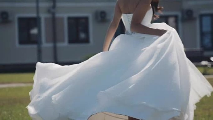 美丽的新娘在婚礼前走到外面。女人穿着婚纱停下来转身。慢动作