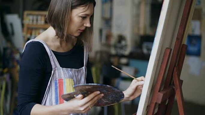 围裙中的年轻画家女孩在美术课上画画布上的静物画
