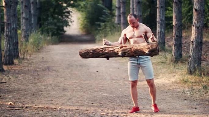 强壮的肌肉男人在森林道路上举起原木
