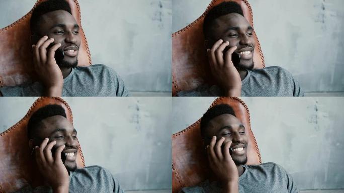 年轻的非洲男性坐在椅子上，在智能手机上聊天的肖像。男人笑着点头同意