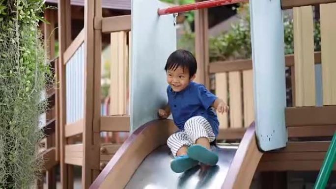 快乐的亚洲小男孩从儿童滑梯上往下走。