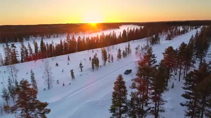 空中: 金色冬季日出时，汽车在白雪皑皑的森林中的乡村道路上行驶