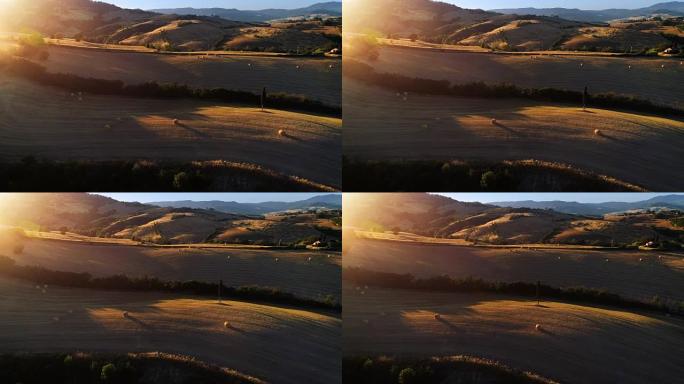 移动空中拍摄收获的田野、树木和山丘。夕阳照亮了美丽的色彩。