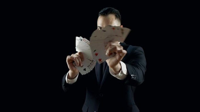 穿着黑色西装的专业魔术师表演纸牌技巧，使纸牌扇出。花招。背景是黑色的。
