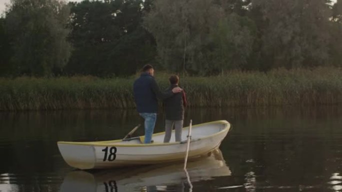 父亲和儿子在钓鱼时站在船上。儿子摆动钓鱼竿。父亲鼓励儿子。