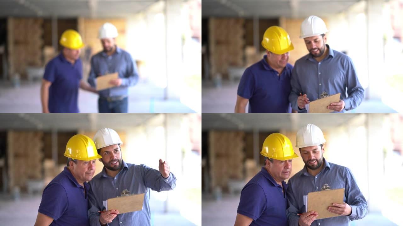 施工经理和工人看着建筑工地，经理拿着剪贴板指着并给出指示