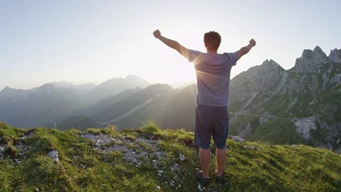 举起手臂的慢动作年轻男性徒步旅行者在日落时欣赏山顶景色