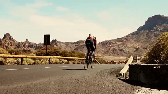 两名骑自行车的人在高速公路上移动的低角度镜头，背景是落基山脉和沙漠。