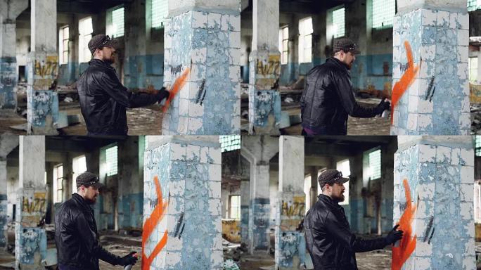 大胡子涂鸦艺术家正在使用气溶胶涂料在旧废弃建筑的柱子上绘画。现代青年亚文化、创意人物与街头艺术观念。