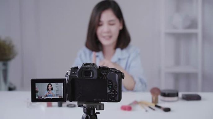 快乐微笑的亚洲女人或美容博主用刷子和相机录制视频，并在家里挥手。美女视频博客博客人物概念。