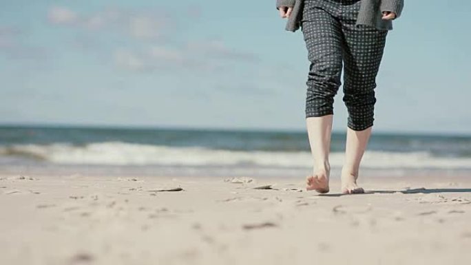 一名孕妇赤脚走在沙滩上，慢慢靠近相机