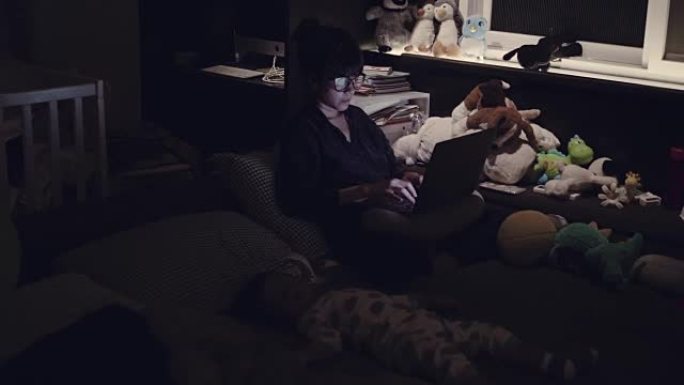 年轻的母亲晚上用笔记本电脑和儿子睡在床上。