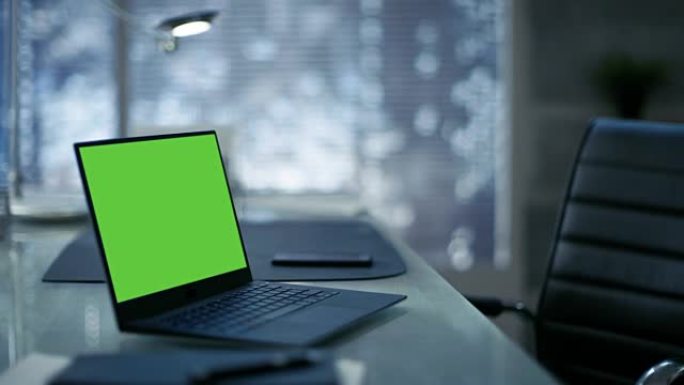带有绿色模拟屏幕的笔记本电脑位于现代简约办公室的桌子上。