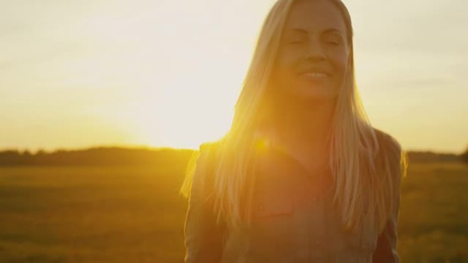 微笑的金发女孩在日落时走在田野上