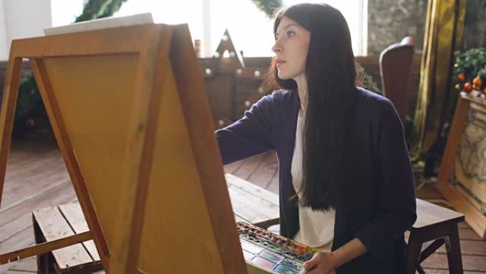 年轻女性艺术家在画架画布上用水彩颜料和画笔绘制画图