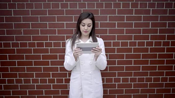年轻漂亮的黑发女子在城市街道上使用数字平板电脑。漂亮的白人女人在白色外套。