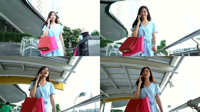 年轻漂亮的女人用手机说话，拿着购物袋走路。