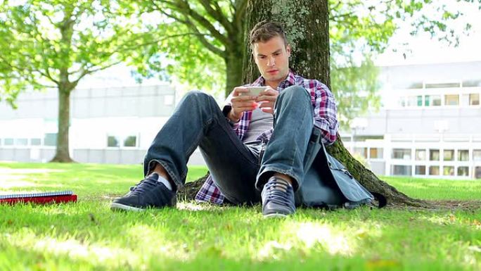 年轻的学生坐在草地上发短信