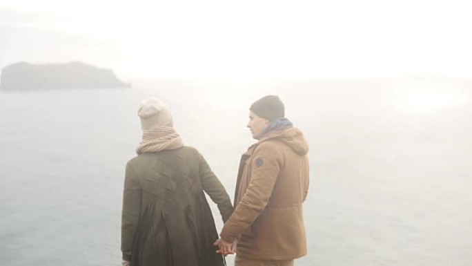 年轻美丽的夫妇站在海边欣赏美景，转身离开