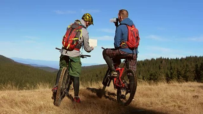 骑在山地自行车上的男性朋友在地图上讨论正确的路线