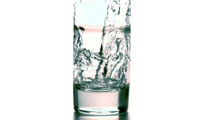 水倒入白色背景的玻璃杯中