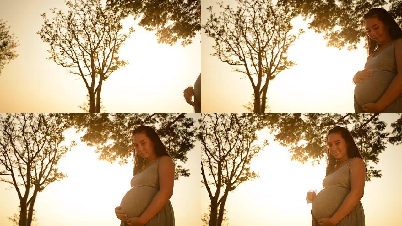 孕妇站立是放松湖畔日落背景
