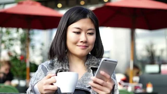 亚洲女人在看短信，人行道咖啡馆。