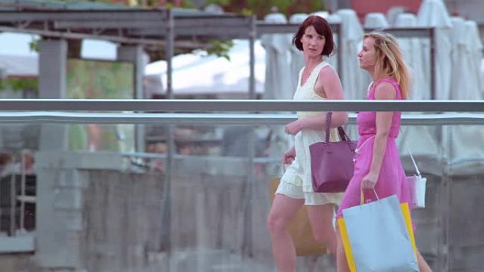 SLO MO女性朋友带着购物袋走过一座桥