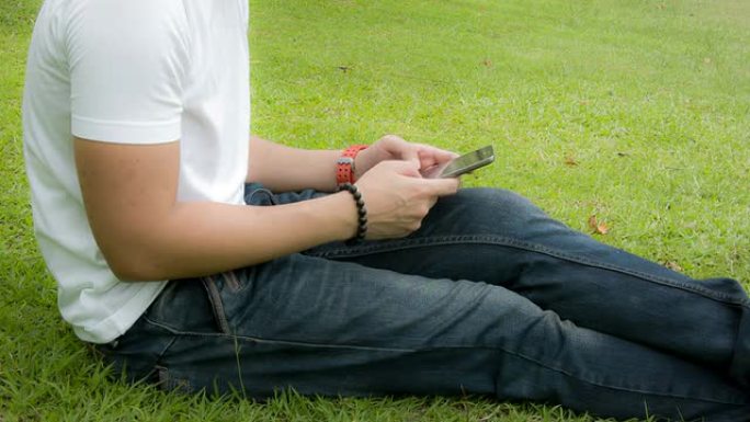 一个拿着智能手机的年轻人坐在草地上。