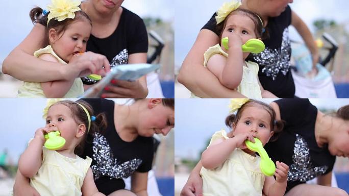 女婴坐在母亲的腿上，咀嚼手机牙器