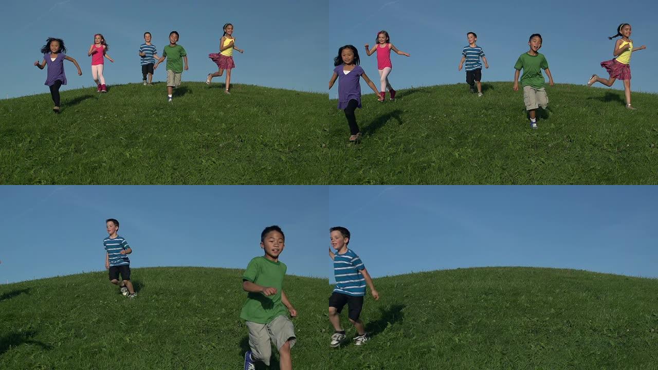 快乐的孩子们以慢动作从长满草的小山上跑下来