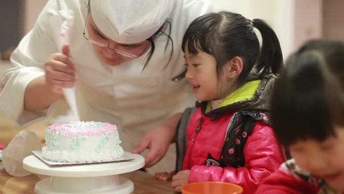 可爱的中国女婴手表厨师在生日蛋糕上滚边奶油