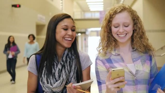 十几岁的高中女生在繁忙的走廊里大笑并使用智能手机