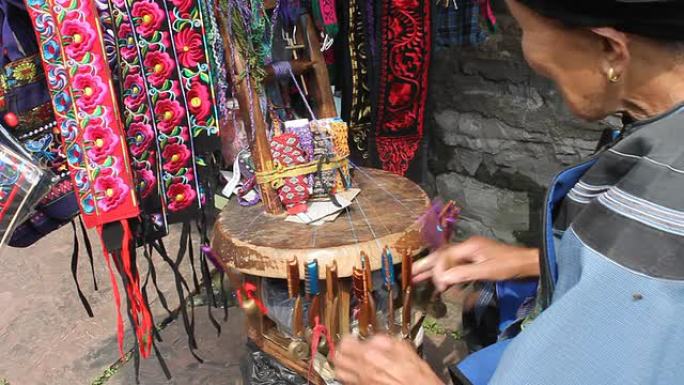 穿着苗族服装的老女人形象迅速编织着传统的乐队。