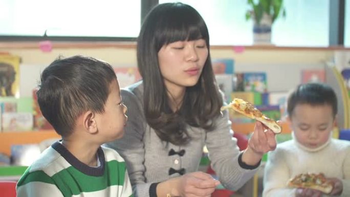 亚洲儿童和学龄前老师在教室里吃披萨