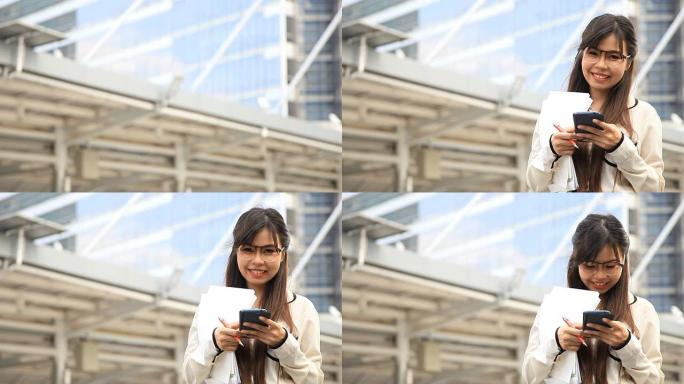 高清：快乐的女商人用智能手机发信息，拿着纸和文件夹。