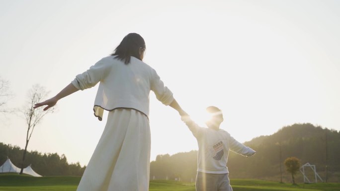 年轻妈妈陪伴孩子草地玩耍大手牵小手转圈圈