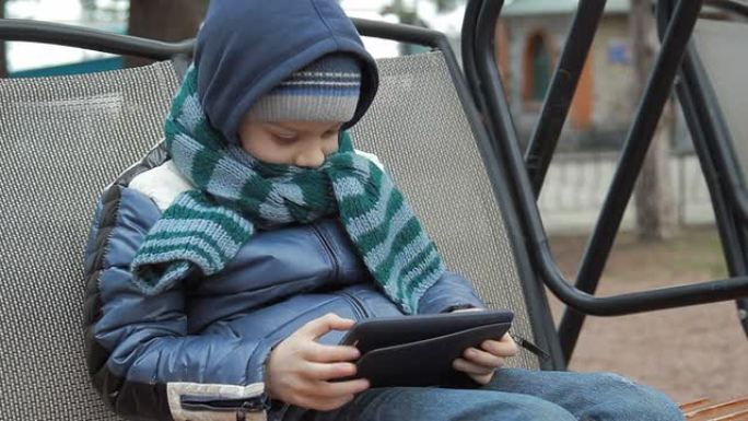 一个拿着数字平板电脑独自坐在秋千上的小男孩