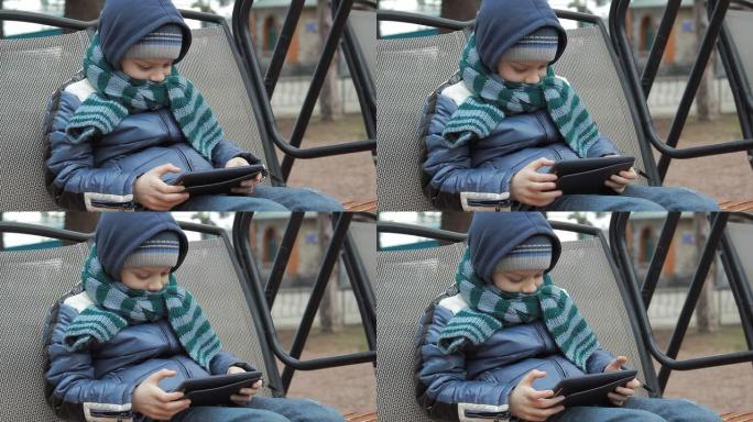 一个拿着数字平板电脑独自坐在秋千上的小男孩