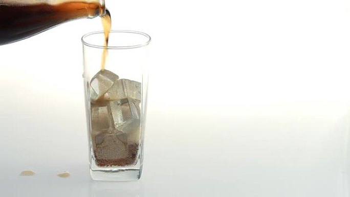往杯子里倒冰块和气泡的可乐。特写汽水。白色隔离的食物背景。