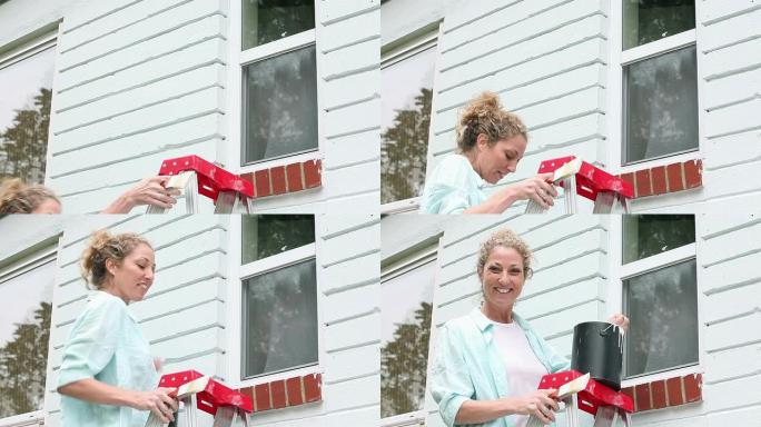 女人爬梯子，准备粉刷房屋外观