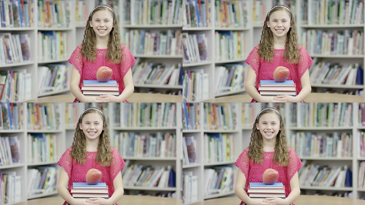 女小学生在图书馆与书籍和苹果合影