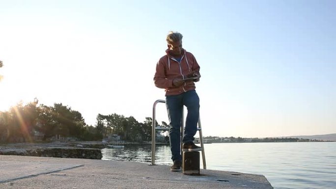 一名男子拿着平板电脑走到海边的码头上拍照