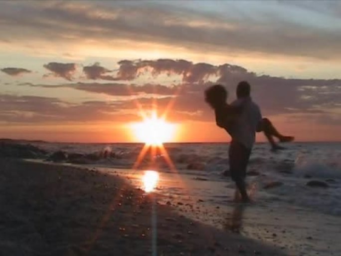 日落时在海滩上玩得开心的夫妇