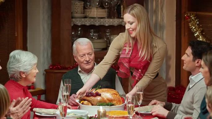 女人将火鸡带到圣诞节餐桌上，家人鼓掌
