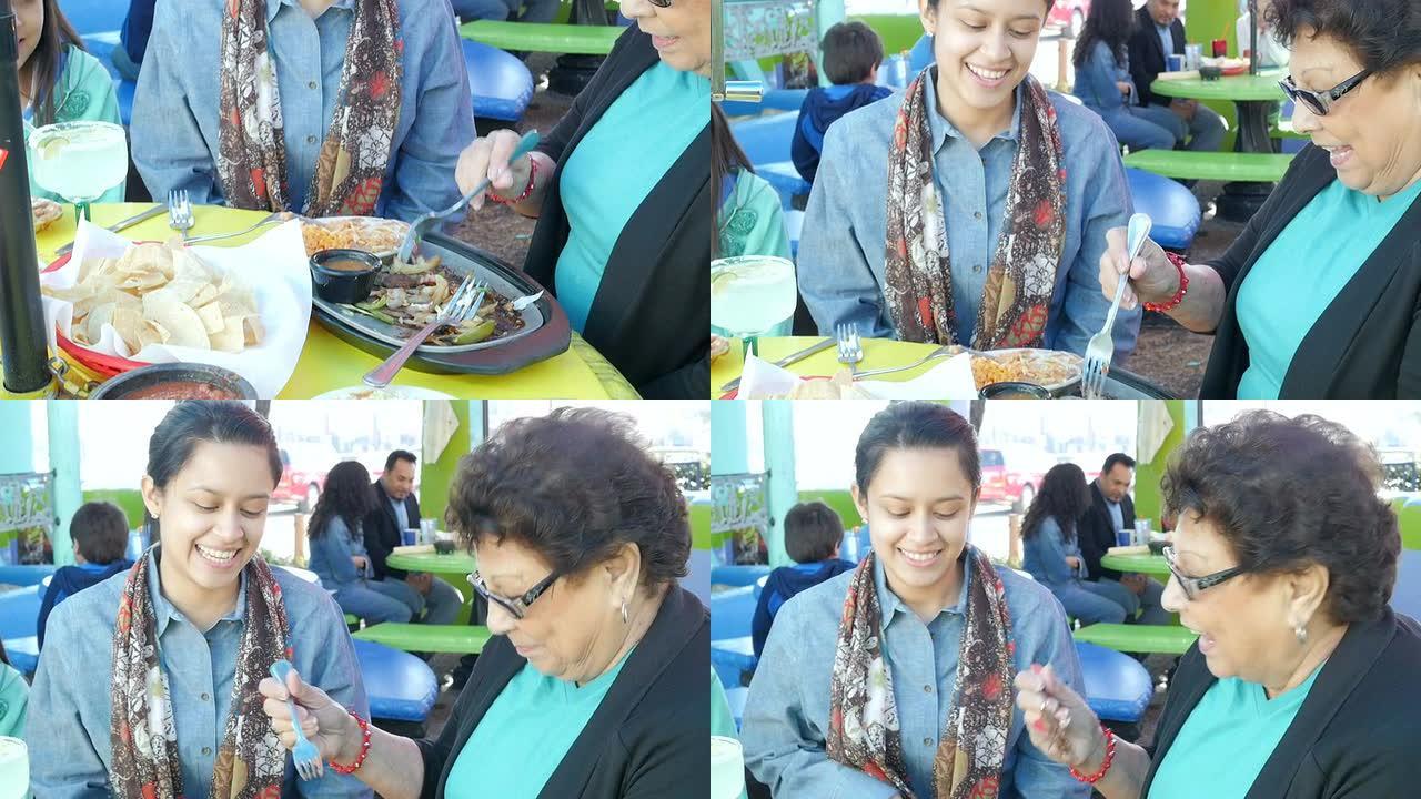 年轻的西班牙裔妇女与祖母在户外餐厅露台上用餐