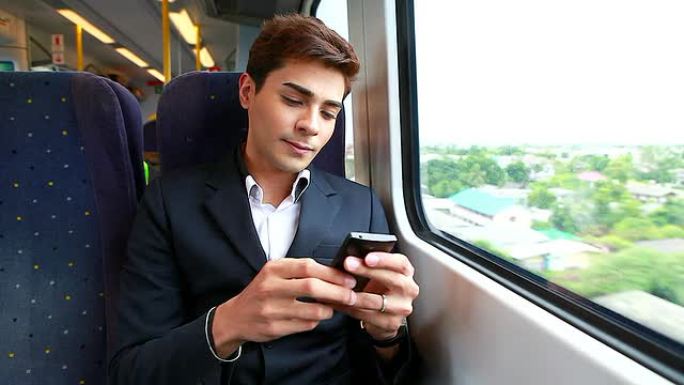 高清: 年轻商人在火车上玩手机。