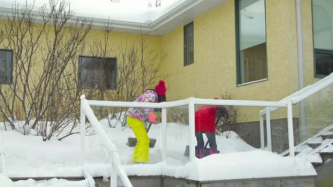 母亲和女儿正在铲房子甲板和台阶上的雪